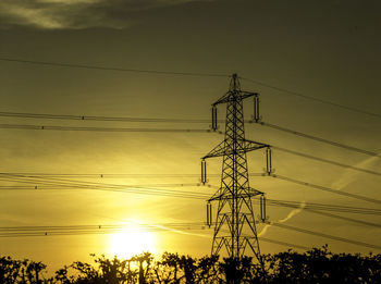 Low angle view of electricity pylon against sky during sunset