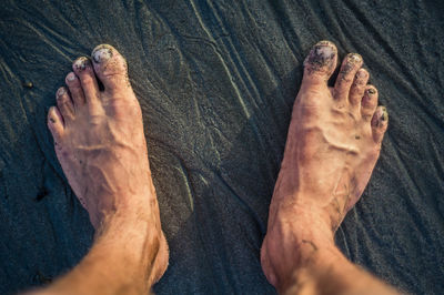 Low section of man standing on wet sand