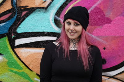 Portrait of smiling woman with pink hair standing against graffiti wall