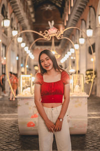 Portrait of smiling young woman standing against illuminated traditional clothing