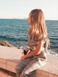 Woman sitting by sea against sky