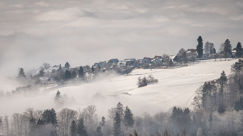 Scenic view of snow covered village on hill against sky