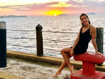 Portrait of smiling young woman sitting by sea during sunset