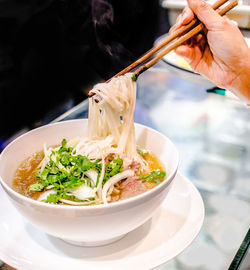 Cropped hand holding chopsticks over soup bowl