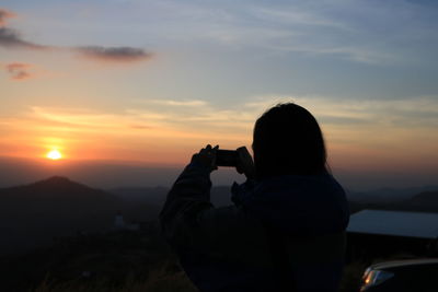 Man photographing at camera against sky during sunset