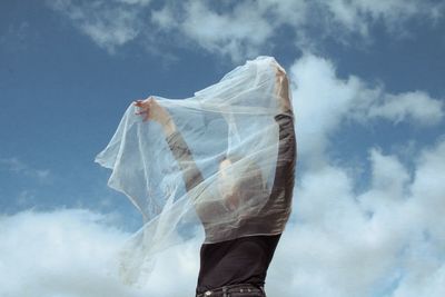 Woman holding white textile while standing against cloudy sky