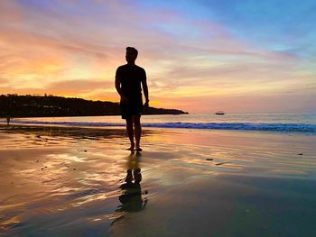 Rear view of man standing on beach during sunset