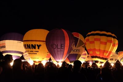 Group of people looking at illuminated hot air balloons against clear sky during night