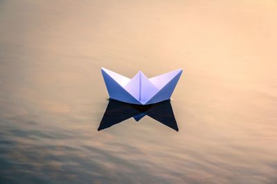 High angle view of white paper boat floating on lake during sunset