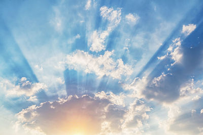 Low angle view of sunlight streaming through clouds