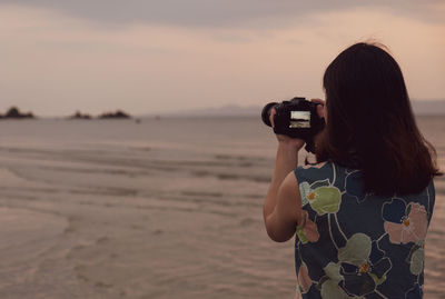  rear view of young woman using camera to take picture of the beach during summer vacation