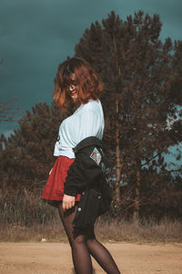 Side view of woman standing by tree against sky