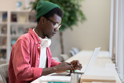 Young african american man freelancer working on laptop using public library as workspace