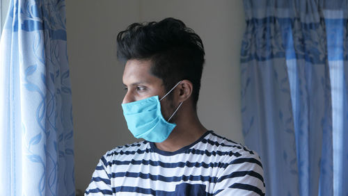 Close-up of man wearing mask looking away while standing at home
