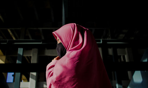 Midsection of woman with pink umbrella standing in corridor