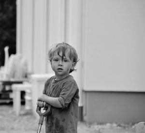 Portrait of cute boy with cropped push scooter standing on footpath