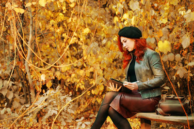 Young woman using mobile phone while sitting on autumn leaves