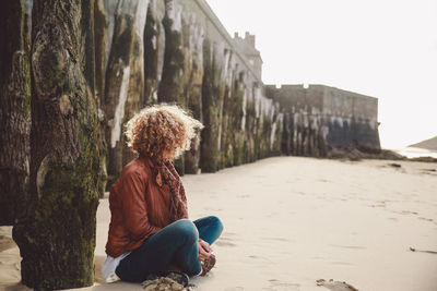 Woman sitting at beach against castle