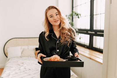 Portrait of young woman holding camera at home