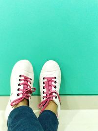 Low section of woman wearing shoes against green wall