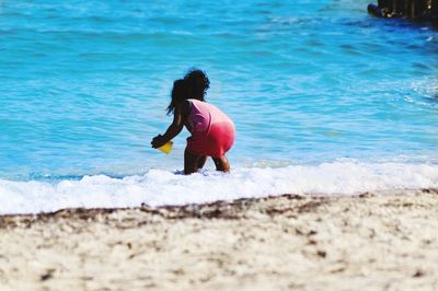 Rear view of girl playing in sea on shore