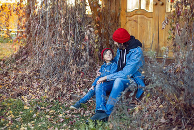 Portrait of village boy child and father in red hats sitting on porch in autumn an abandoned house