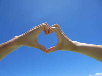 Cropped couple making heart shape against blue sky during sunny day