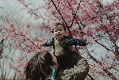 Mother lifting cute daughter against tree