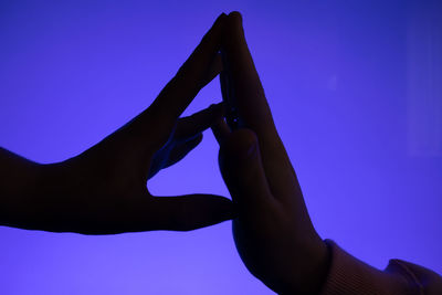 Silhouette image of touching hands against blue background