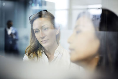 Serious businesswomen working in office with male colleague in background seen through window