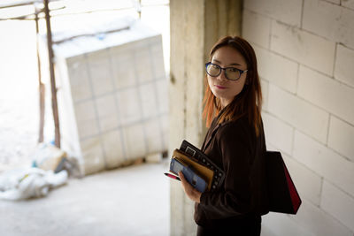 Portrait of young businesswoman with calculator standing in building at construction site