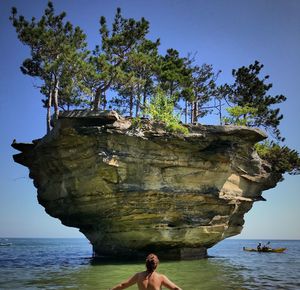 Man standing on rock by sea against clear sky
