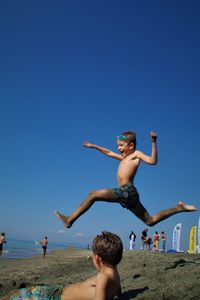 People jumping on beach against clear blue sky