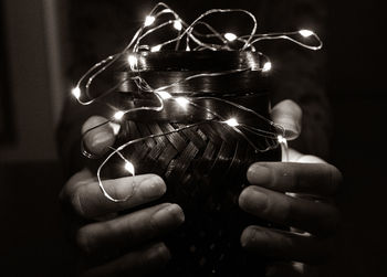 Cropped hands of person holding illuminated lighting equipment and wicker container