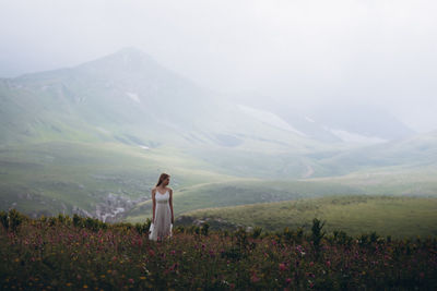 Woman sanding on field against mountains and sky