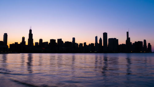 Sea by buildings against sky during sunset