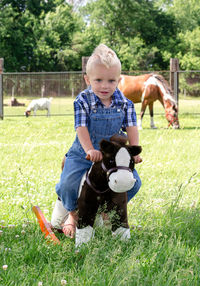 Little boy on a rocking horse with real horse behind him
