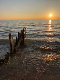 Wooden posts on beach against sky during sunset