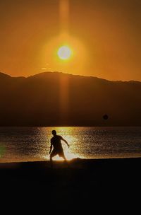 Silhouette man standing at beach against sky during sunset