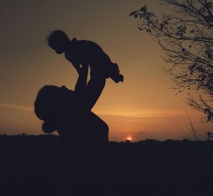 Silhouette woman lifting baby against sky during sunset