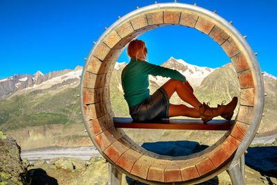 Full length of woman sitting by wooden circle against sky