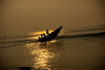 Silhouette man in sea against sky during sunset