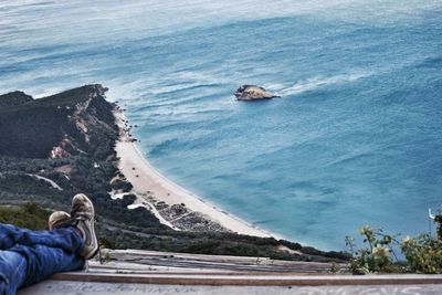 Low section of man sitting by sea against sky