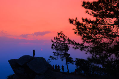 Silhouette man standing on rock against sky during sunset