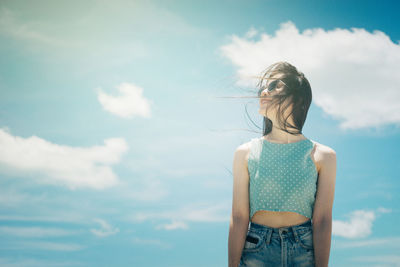 Young woman wearing sunglasses standing against sky