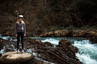 Woman wearing virtual reality simulator while standing against trees