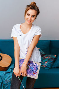 Portrait of a smiling young woman holding camera at home