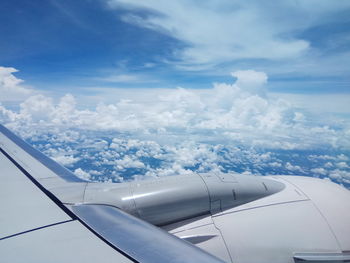 Close-up of airplane wing over cloudscape against sky