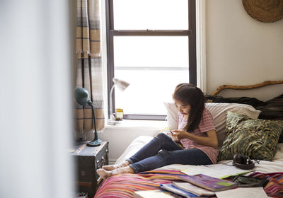 Teenage girl using smart phone while sitting on bed