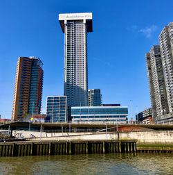 Modern buildings by river against blue sky